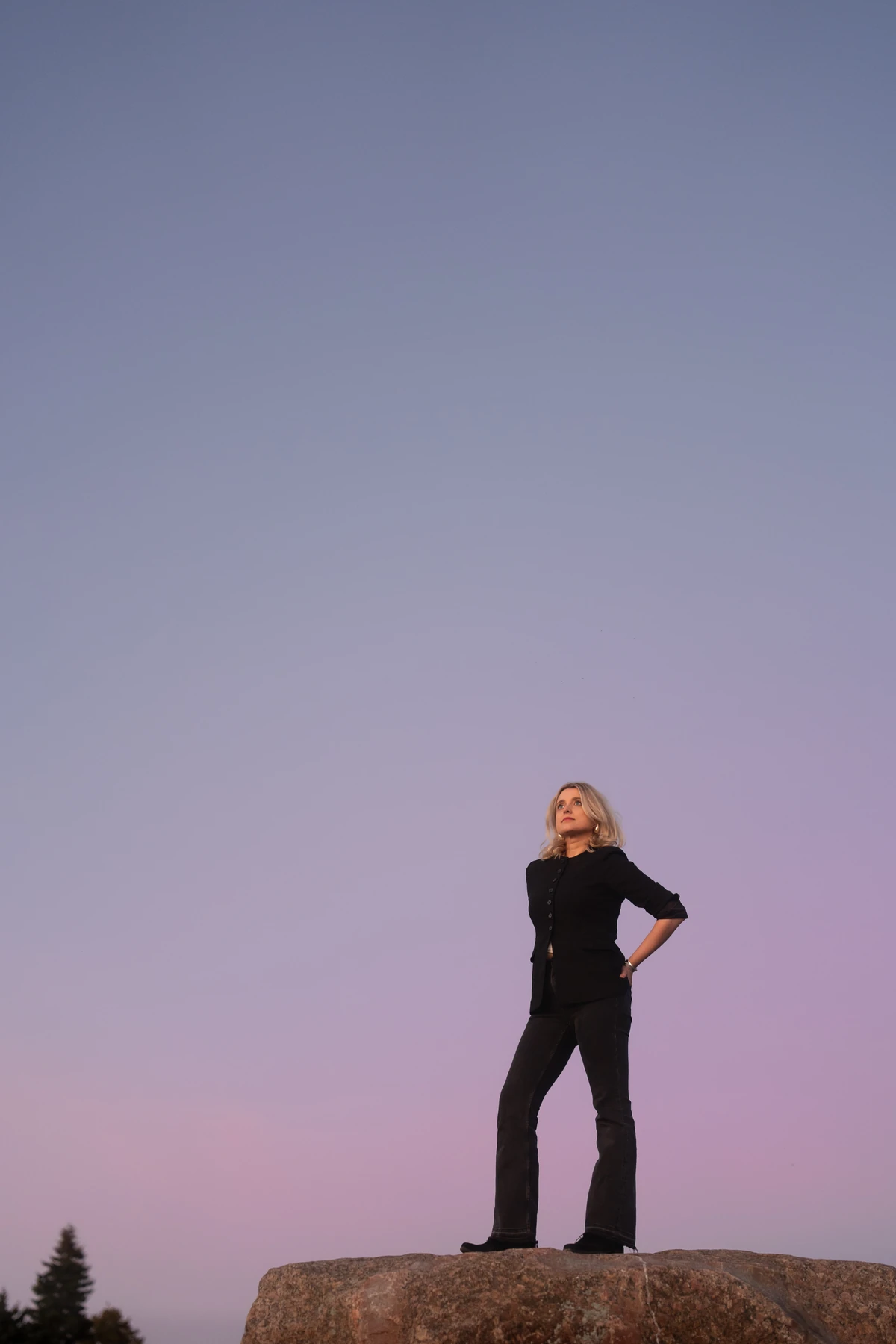 Joanna Numminen, founder of Numminen Advisory, standing on a seaside rock against a pink dusk sky in Helsinki