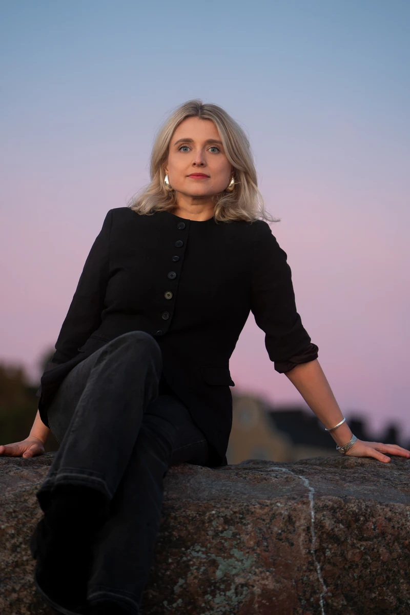 Joanna Numminen, founder of Numminen Advisory, seated on a granite rock at dusk in Helsinki
