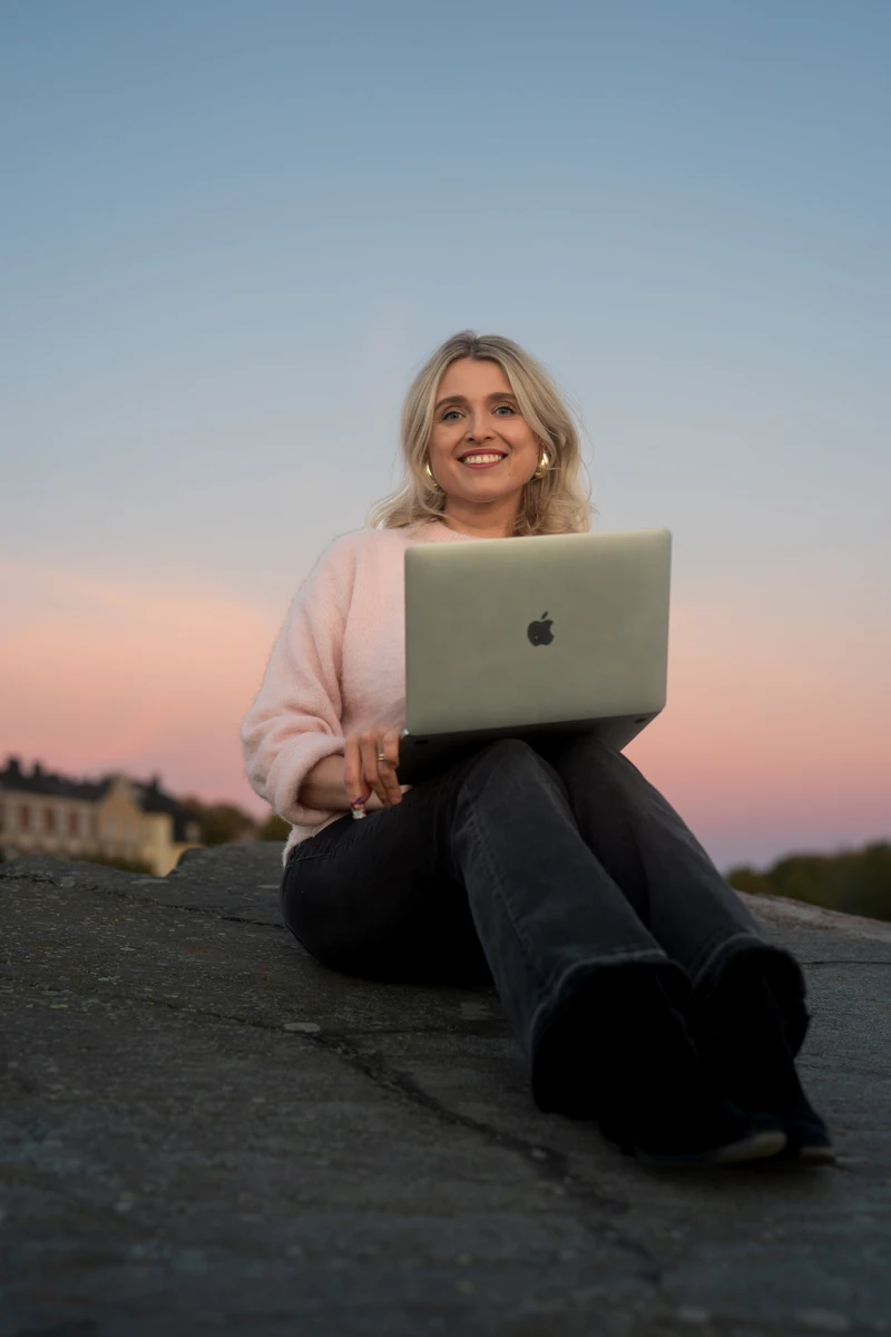 Joanna Numminen, founder of Numminen Advisory, working on her laptop on a seaside rock at dusk in Helsinki
